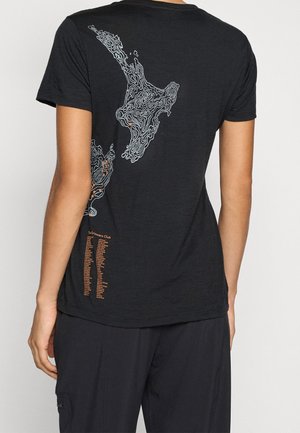 Person iført en sort t-shirt med et hvidt topografisk kort-design og orange tekst, der viser navne på den nedre ryg.