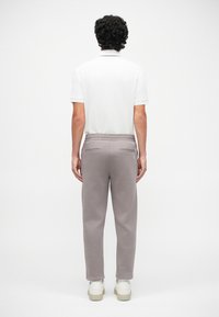 Cămașă polo albă cu mâneci scurte, asortată cu pantaloni de trening deschiși la culoare, cu buzunare laterale. Modelul poartă adidași albi.
