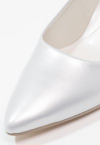 Gros plan sur la partie à bout pointu d'une chaussure plate pour femmes brillante argentée avec une texture lisse et une doublure intérieure beige clair.