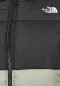 Czarna kurtka puchowa z jasnoszarym dolnym panelem, z zamkiem błyskawicznym z przodu oraz białym logo "THE NORTH FACE" na górnej części klatki piersiowej.