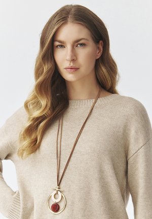 Beige sweater with rounded neckline and long sleeves, featuring a long brown cord necklace with gold and red circular pendants.
