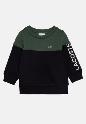 Dziecięca bluza z długim rękawem z ciemnozieloną górną częścią, czarną dolną częścią, ściągaczami na mankietach, logo Lacoste na piersi oraz nazwą marki na rękawie.