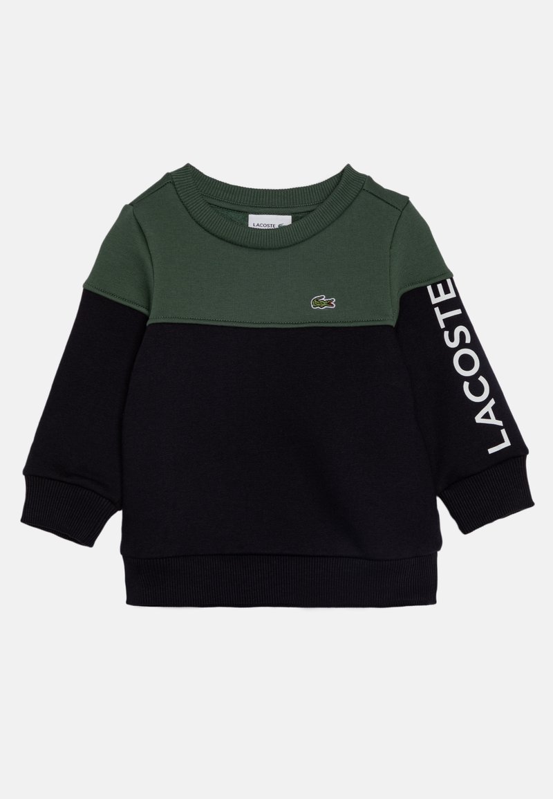 Sweat-shirt à manches longues pour enfants avec une section supérieure vert foncé, une section inférieure noire, des poignets côtelés, le logo Lacoste sur la poitrine et le nom de la marque sur la manche.