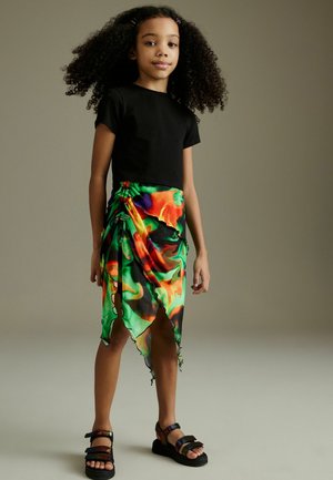 Černý crop top, barevná mramorovaná sukně s rovnou siluetou v zelené, oranžové a fialové barvě s nepravidelným lemem; masivní černé sandály s nastavitelnými popruhy.