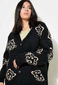 Mustavillainen neuletakki, jossa on leopardikuvio vaaleassa sävyssä, V-pääntie, napitus ja tekstuuri.