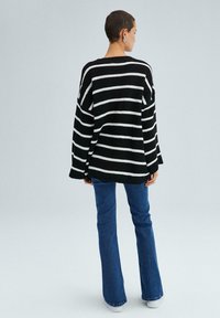 Randig tröja i svart och vitt, stickad textur, oversize passform, lösa ärmar. Kombination med svagt utsvängda blå jeans och vita skor.