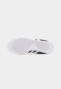 Μαύρη και λευκή σόλα από αθλητικό παπούτσι Adidas με μοτίβο από εξαγωνική πέλμα και το λογότυπο της μάρκας ορατό σε λευκό φόντο.