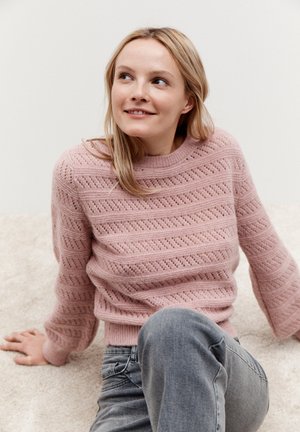 Helles rosa gestricktes Sweatshirt mit strukturiertem Muster, runder Ausschnitt und weiten Ärmeln, kombiniert mit grauen Jeans. Sanfter Hintergrundtextur.