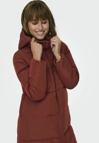 Veste en duvet bordeaux avec capuche, fermeture éclair et design matelassé. Équipée de poignets élastiques et d'un matériau léger et élégant.