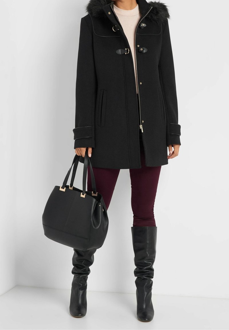 Svart ullrock med fuskpäls på huva, guldfärgad hårdvara och sidofickor. Matchas med bordeauxfärgade byxor, svarta höga stövlar och en strukturerad väska.