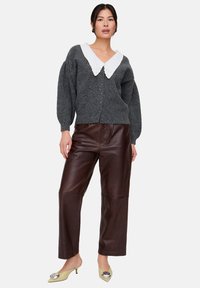 Graue Strickjacke mit weißem Spitzenkragen, kombiniert mit braunen Lederhosen und hellgelben mules mit Absatz und metallischen Akzenten.