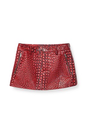 Minigonna rossa in ecopelle effetto coccodrillo con tasche a zip frontali e passanti per cintura su sfondo bianco.