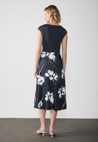 Marineblaues Kleid mit kurzen Ärmeln, tailliertem Oberteil und ausgestelltem Rock. Blumiges Muster in Weiß und Schwarz. Schlicht, über Knielänge.