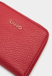 Cartera de cuero texturizado rojo con herrajes dorados y logo grabado "LIUJO". Presenta un cierre de cremallera y una forma rectangular estructurada.