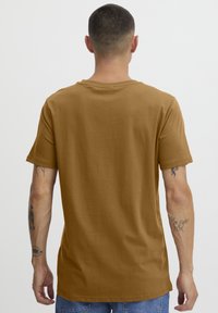 Brun bomull T-skjorte med korte ermer og rund hals, med en avslappet passform. Bakvisningen viser en jevn tekstur og enkelt design.