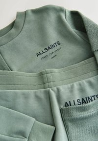 Sudadera y pantalones verdes con puños acanalados, detalles texturizados y "ALLSAINTS" impreso en azul oscuro en la parte delantera. Material suave.