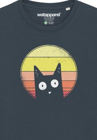 Donkerblauwe T-shirt met een cartoon zwarte kat met grote witte ogen, geplaatst tegen een gestileerde gele en oranje zonsondergang als achtergrond.