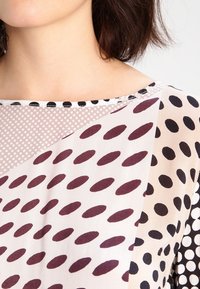 Blusa caratterizzata da una combinazione di motivi a pois in bordeaux, nero e bianco, con un design a strati e un collo rotondo.