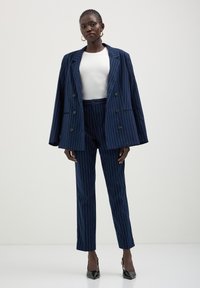 Costume marine à rayures avec un blazer croisé et un pantalon ajusté. Associé à un haut blanc et des escarpins noirs à bout pointu.