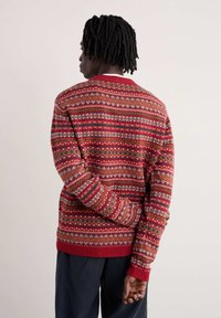 Sarkanais adīts svārks ar daudzkrāsainu rakstu dizainu, ieskaitot ģeometriskas formas un svinīgus motīvus. Ribota apakšmalu un piedurkņu dizains, teksturēta auduma.