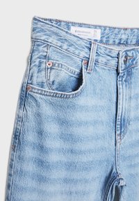 Jean denim bleu clair taille haute avec poches avant, passants de ceinture, bouton en métal et étiquette visible de la marque Stradivarius à l'intérieur de la ceinture.