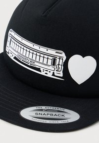 Black snapback cap with a white graphic of a tram labeled "Carhartt WIP" next to a solid white heart shape.