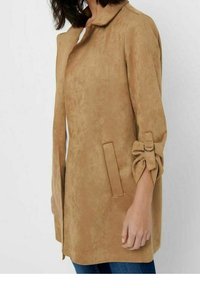Tan väristä keinonahkakangasta takki, jossa on kaulus, sivutaskut ja rullatut hihat, jotka on kiinnitetty soljella. Sujuva pinta ja suora leikkaus.