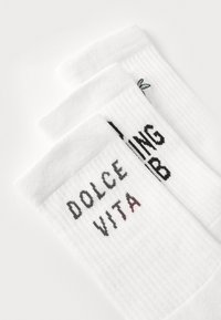 Valged sokid, millel on soonikkoes ja mustad ning punased kiri. Ühel sokil on kirjas "DOLCE VITA" ja teisel "LIVING."