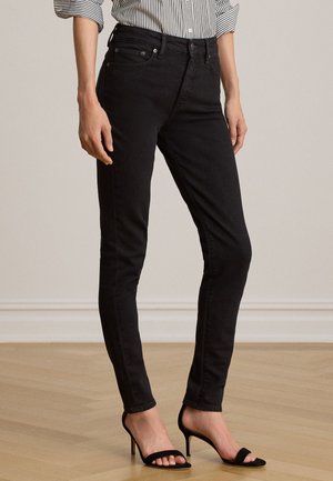 Donna con jeans skinny neri, tacchi alti neri open toe e camicia a righe maniche lunghe con le maniche arrotolate.