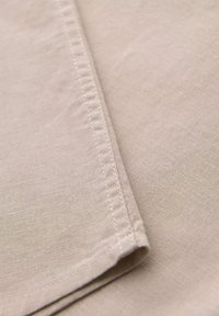 Lichtbeige linnenstof met een gladde textuur, gekenmerkt door net afgewerkte randen en een subtiele glans. De stof ligt plat en toont zijn zachtheid.