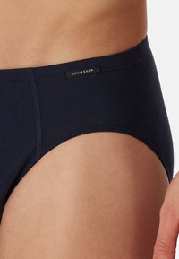 Marineblaue Baumwollslips mit glatter Textur, seitlichen Nähten und einem schwarzen Markenlabel an der Taille. Klassisches Schnittdesign für eine optimale Passform.