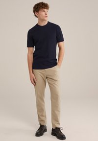 Navy short-sleeve knit t-shirt paired with beige chinos and dark brown lace-up shoes. Casual fit with ribbed neckline and sleeves.
