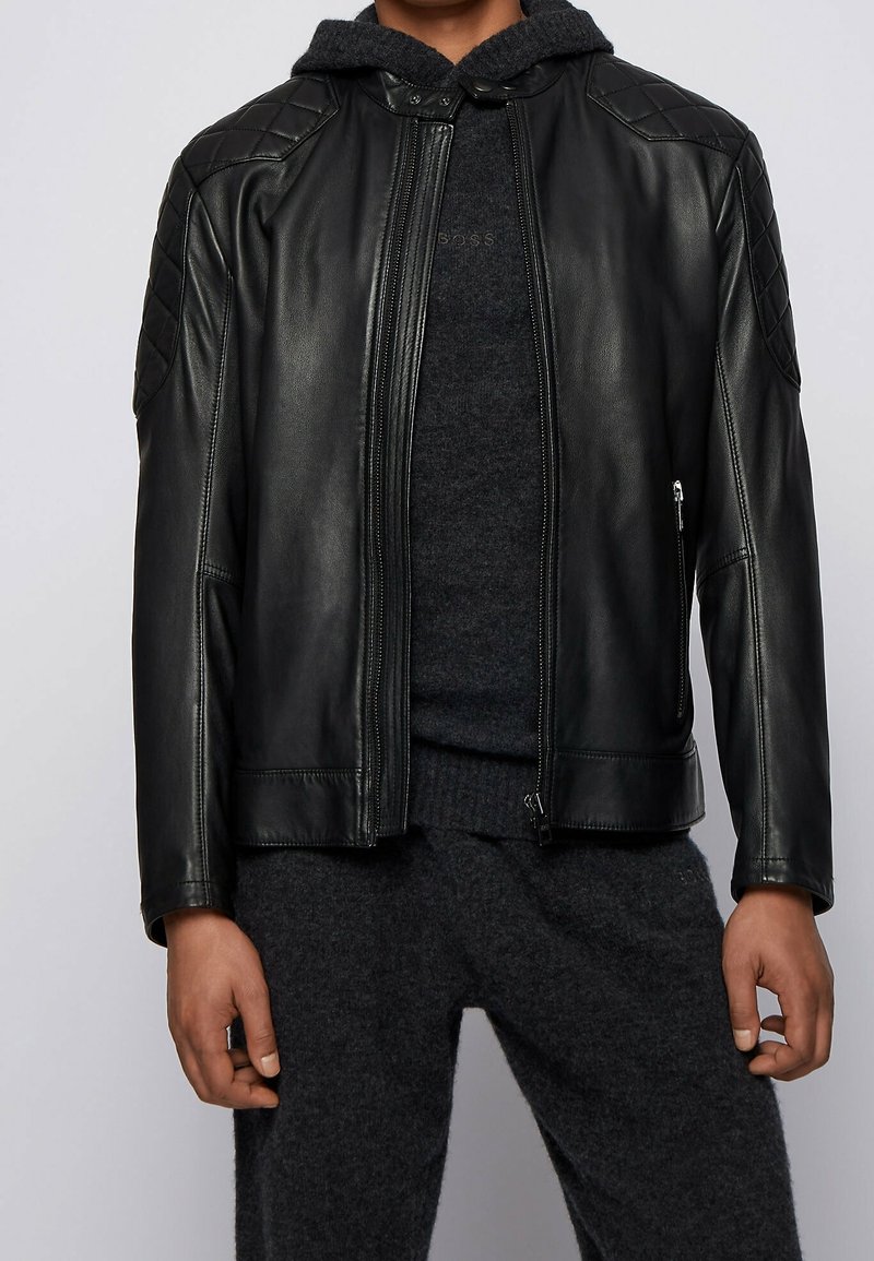 Černá kožená bunda s prošívanými akcenty na ramenou, zapínáním na zip a mikinou pod ní. Texturovaná tkanina, přiléhavý střih a přední kapsy.