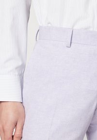 Helle lila Hosen aus Leinen mit glatter Textur, ausgestattet mit einem taillierten Bund und Seitentaschen, kombiniert mit einem kontrastierenden gestreiften Hemd.