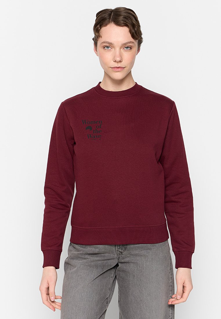 Sweatshirt bordeaux à col rond, à manches longues et avec des poignets côtelés. Présente un texte graphique noir "Femmes des vagues" sur la poitrine.