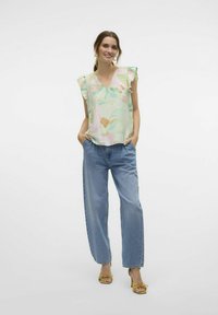 Ziedu raksta, gaiši zaļa blūze ar viļņotām piedurknēm, apvienota ar augsto jostu brīvā stila džinsiem un sinepju dzeltenām kurpēm ar augstu papēdi.