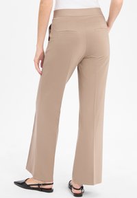 Beige weite Beinhosen aus einem glatten, elastischen Stoff, mit Gesäßtaschen und einem bequemen Bund. Getragen mit schwarzen Absatzsandalen.