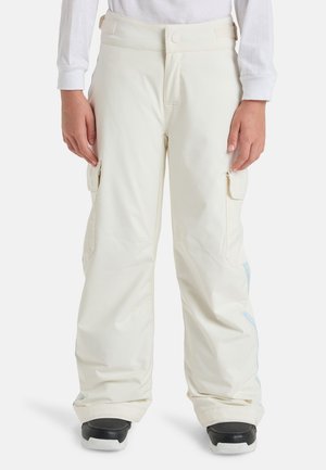 Personne portant un pantalon cargo blanc ample avec poches à rabat et des chaussures noires et blanches, debout les mains détendues le long du corps.
