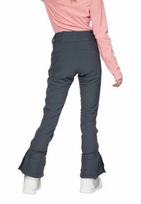 Harmaat hiihtohousut, joissa on slim fit -suunnittelu, vetoketjut nilkoissa ja vahvistetut saumat, yhdistettynä valkoisiin ja harmaisiin jalkineisiin.