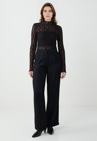 Top nero a maniche lunghe con un design trasparente e testurizzato. Abbinato a pantaloni neri a vita alta, creando un silhouette sartoriale.