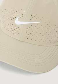 Bežna kapa s perforiranim dizajnom, s bijelim Nike logotipom sprijeda, šivenim detaljem i zakrivljenim vizorom. Meka tkanina.