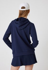 Mörkblå hoodie med dragsko i huvan, ribbade ärmslut och nederkant. I kombination med en matchande utsvängd kjol som visar en avslappnad outfit.
