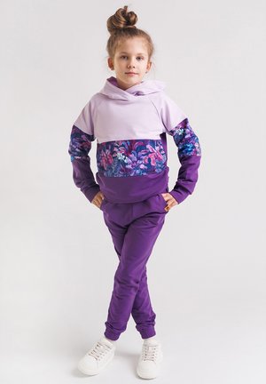 Fioletowy dres składający się z lilakowego, krótkiego hoodie z kwiecistymi akcentami oraz fioletowych spodni. Materiał jest gładki, z elastycznymi mankietami i detalem z logo.