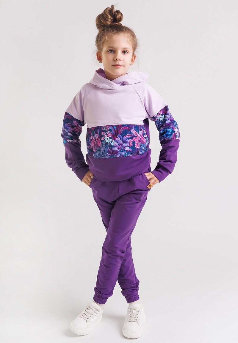 Fioletowy dres składający się z lilakowego, krótkiego hoodie z kwiecistymi akcentami oraz fioletowych spodni. Materiał jest gładki, z elastycznymi mankietami i detalem z logo.