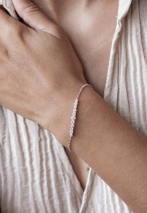 Silver bracelet with a delicate chain featuring clear, faceted stones in varying sizes, showing a subtle sparkle against a textured background.