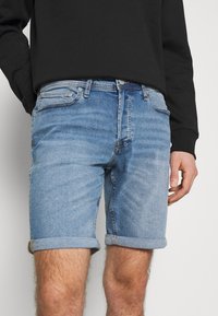 Vaaleansiniset farkkushortsit, joissa on käännetyt lahkeet, viisi taskua ja napitettava etulukitus. Sileä pinta, jossa on haalistumismalleja.