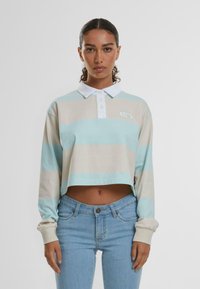 Polo à manches longues coupé en rayures bleu clair et beige, avec un col blanc, une patte de boutonnage et un logo brodé. Jeans en denim.