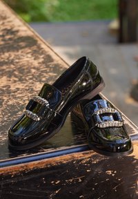 Mocassins en cuir verni noir avec une boucle en métal argenté décorative, au design épuré, bout arrondi et semelle discrète. Intérieur en imprimé léopard texturé.