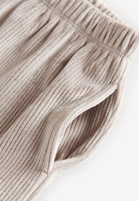 Hellbeige gerippter Stoff mit weicher Textur, ausgestattet mit einem gerafften Bund und seitlichen Taschendetails. Geeignet für legere Outfits.