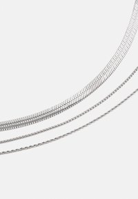 Tre catene d'argento disposte orizzontalmente: una catena a spina di pesce piatta, un design a corda attorcigliata e una catena con maglie tonde lisce.